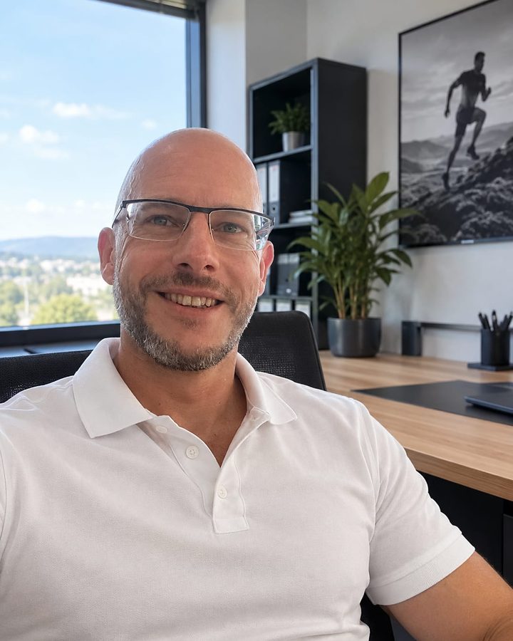 Andreas Flohrmann sitzt lächelnd an seinem Schreibtisch im Büro